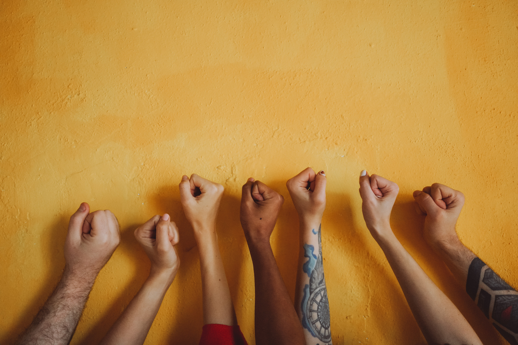 Diverse Hands in Fists on Yellow Wall